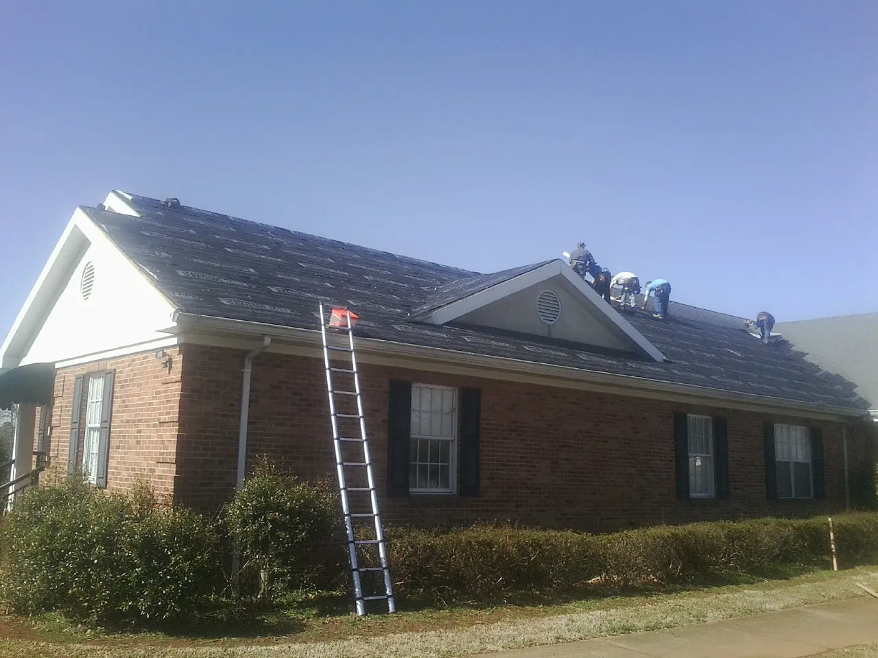 Crew tearing shingles off a brick ranch roof with a ladder set — Metal Roof Repair work by our crew in Fishersville