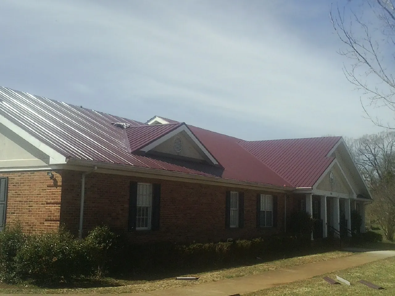 Red metal roof with gabled entries on a long brick building, from a Hail Damage Roof Repair job in Fishersville