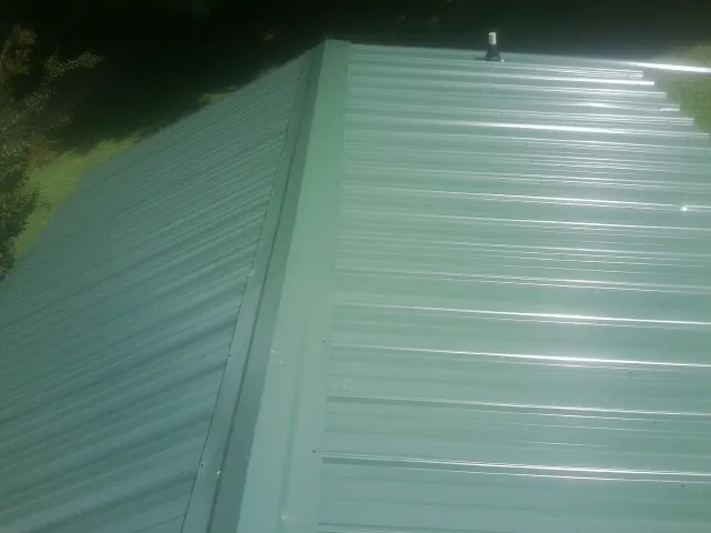 New green metal panels meeting at the ridge of a roof — Flat Roof Repair work by our crew in Fishersville