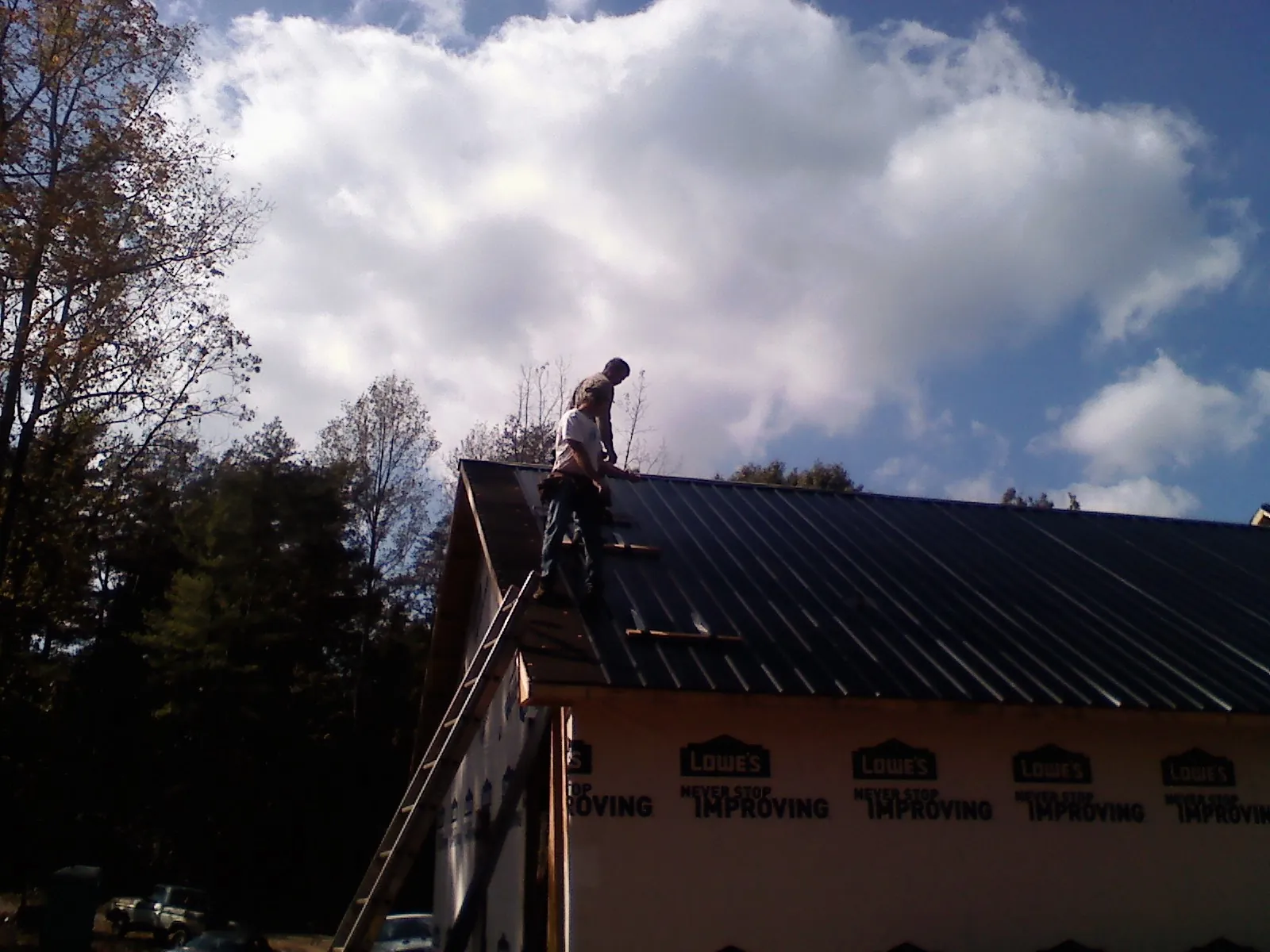 Roofer fastening dark metal panels high against a cloudy sky, from a Roof Inspection job in Fishersville