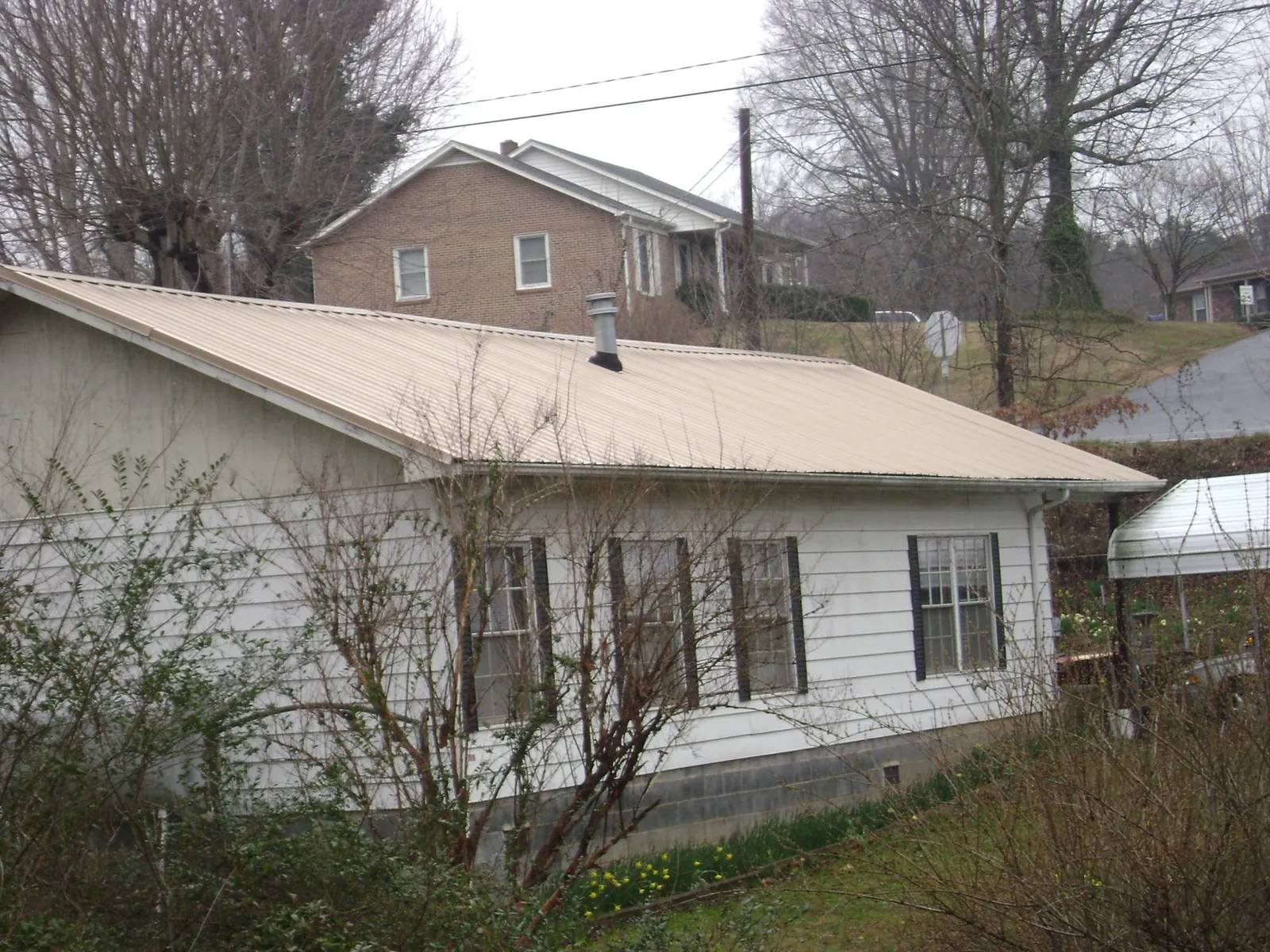 Tan metal roof on a white sided house set into a hillside — Commercial Roofing by Roofing Brothers in Fishersville